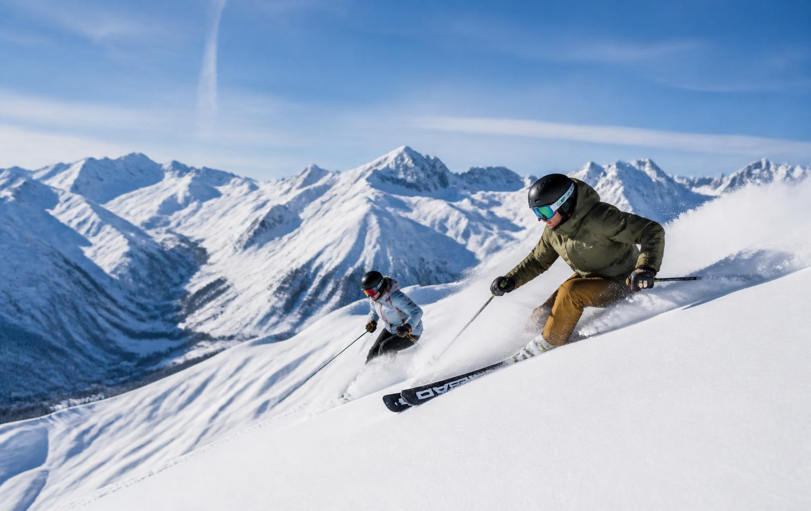 Deux skieurs en pleine descente dans la poudreuse face au panorama alpin